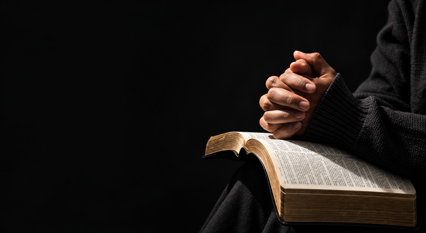 Hands folded in prayer resting on an open Holy Bible